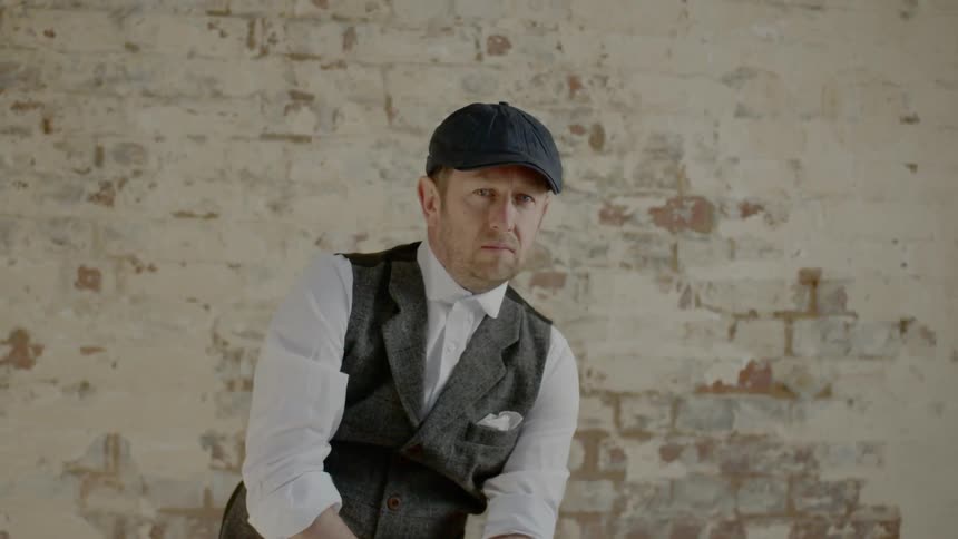 A man in a vest sitting around in front of a wall