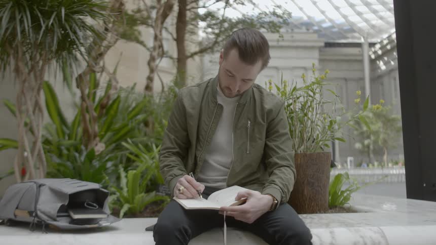 A man sits in an indoor garden and writes in a notebook
