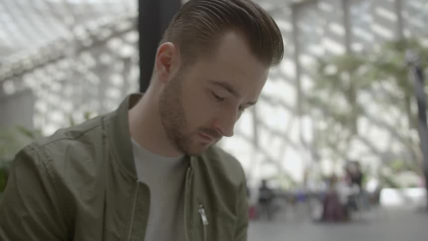 A white man with slicked back hair sits in an open brightly lit room