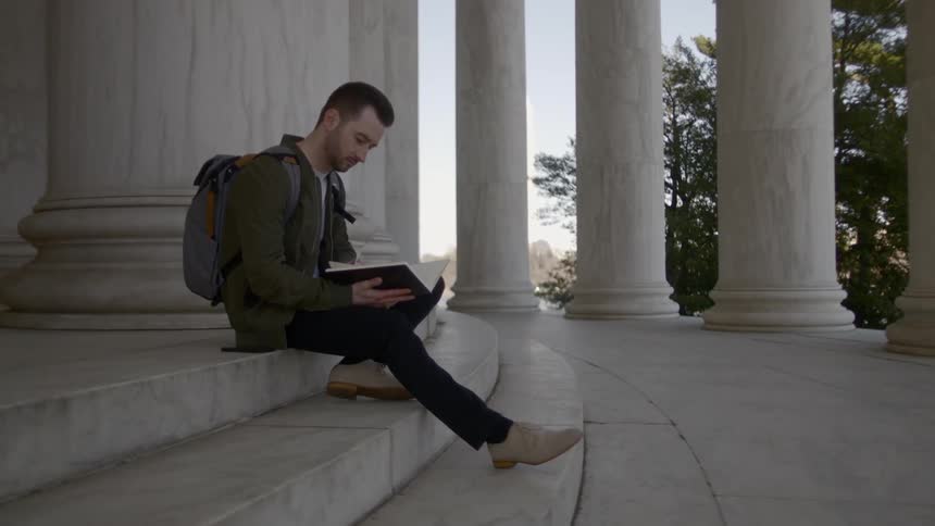 A young man sits on a step and reads a book