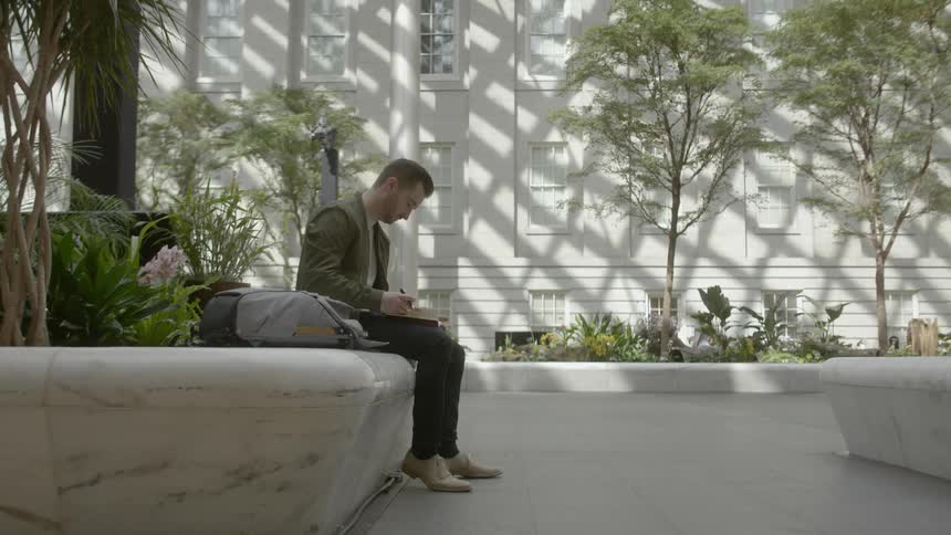 A man sits in a courtyard garden writing in a notebook