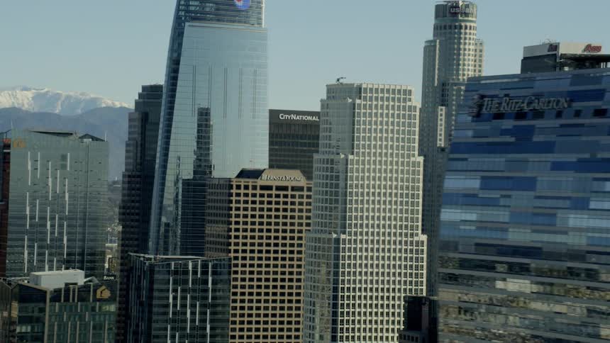 Light reflects off skyscrapers in a city with a mountain ridge on the horizon