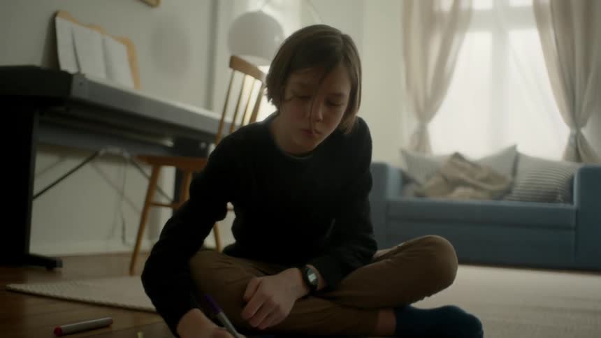 A young boy sits on the floor and colors