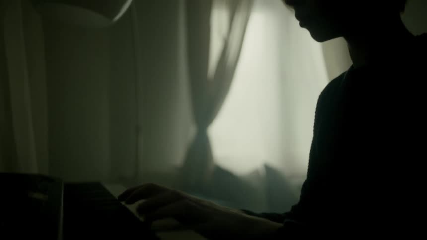Boys silhouette plays the piano in dark room