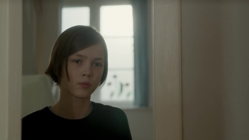 A young white child opens a door and looks through
