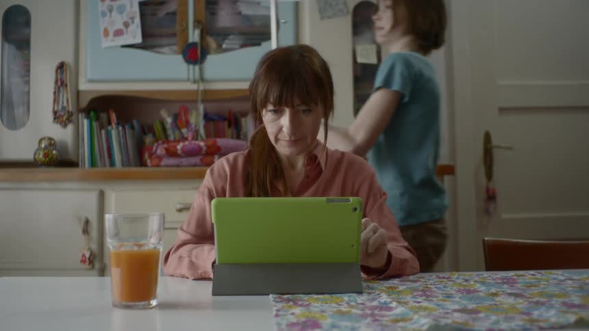 A woman sitting at a table with a girl behind her picking up a lamp