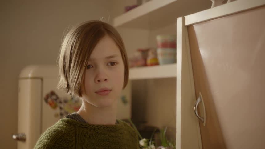 A girl in the kitchen walking up to a cabinet then turning around