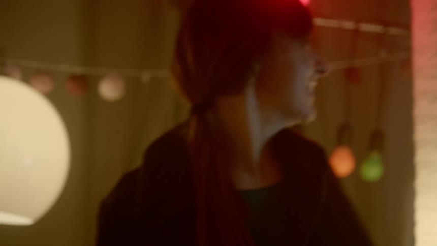 A woman standing over to men dancing with different color lights in the background