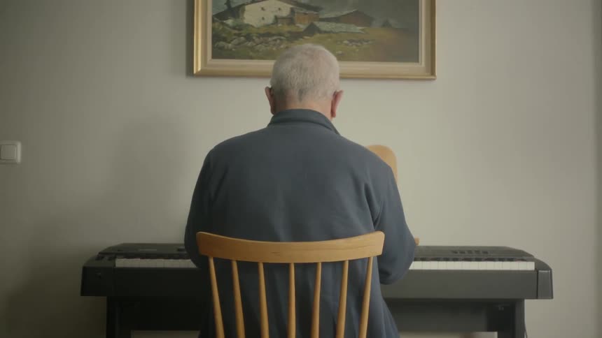 Old man plays the piano and takes off the hearing aid in a room
