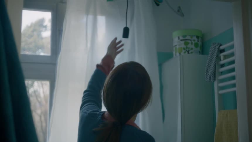 A woman enters a small room to check on an electrical plug hanging from the ceiling