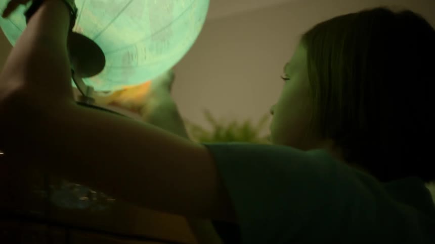 A girl grabbing a globe off of a table