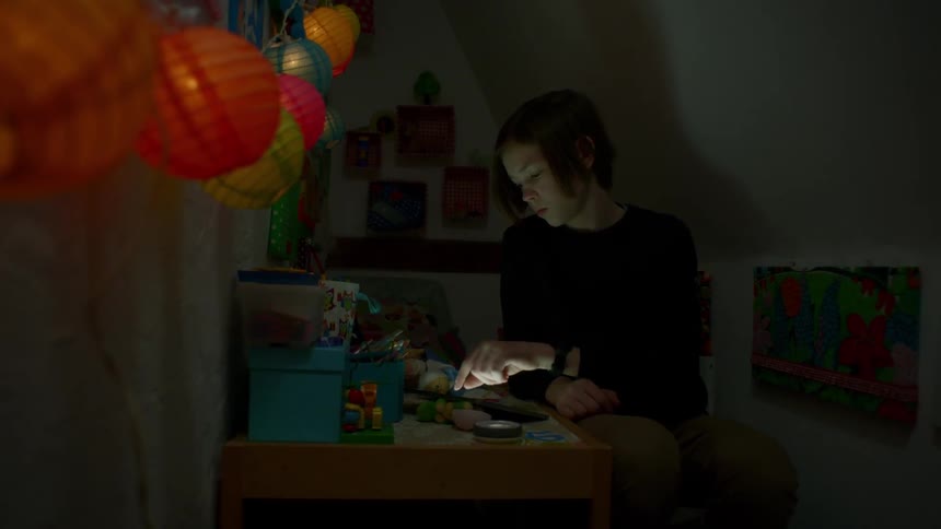 A boy sitting at a desk in a dark room swiping a tablet