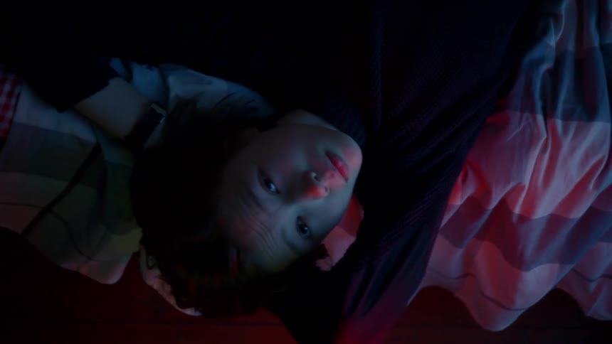 A teen lying on his bed looking up at the ceiling as colored lights glow