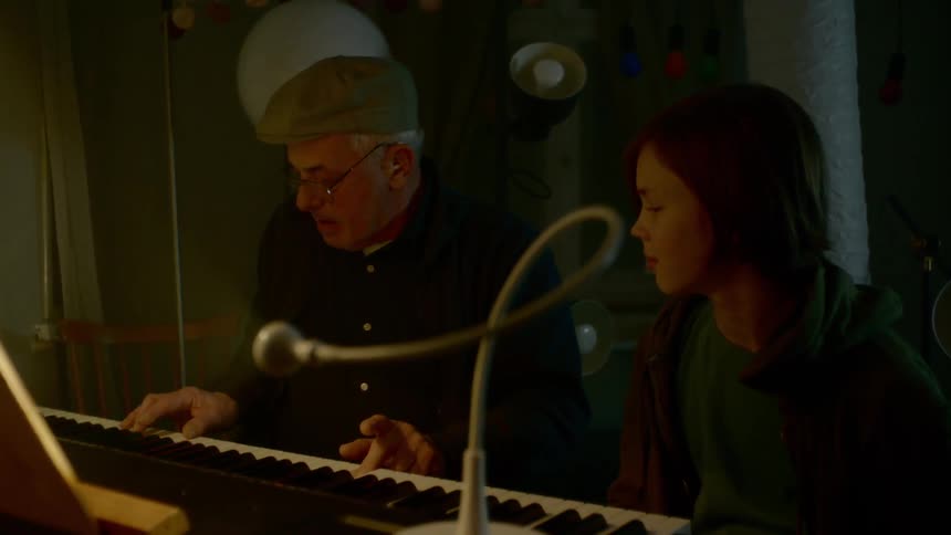 An old man sits with a young boy in front of a piano that is configured to operate light bulbs that are installed behind them