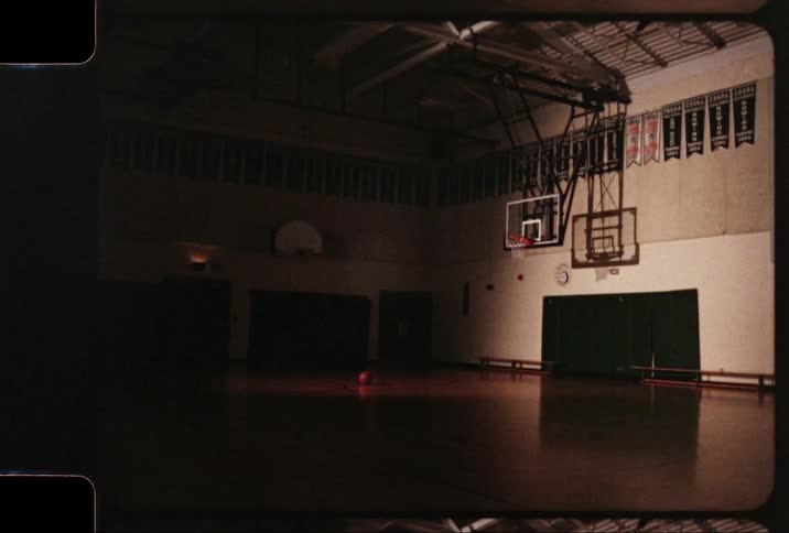 A gymnasium with basketball hoop is dark and empty
