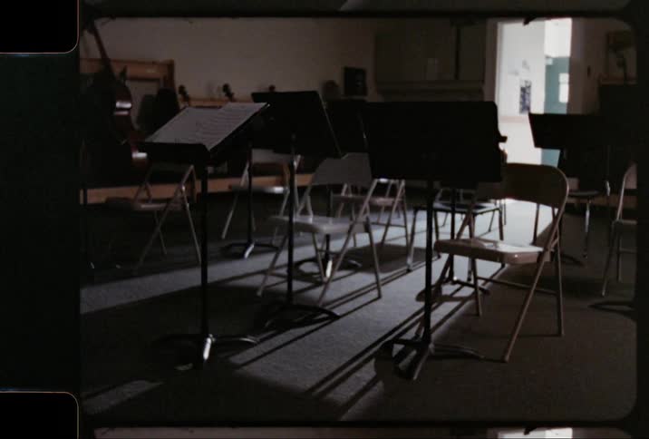 Archival footage shows music pedestals and folding chairs in a music classroom