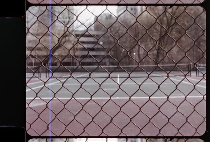 Outdoor tennis courts in a city visible through a chain link fence
