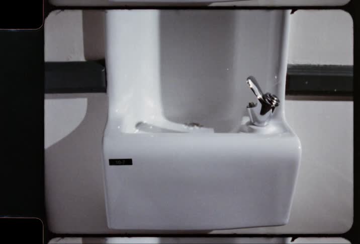 A white drinking fountain with a shiny metallic spout is attached to a wall
