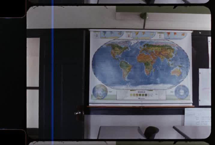 Inside of a classroom a map of the world hangs top a chalkboard