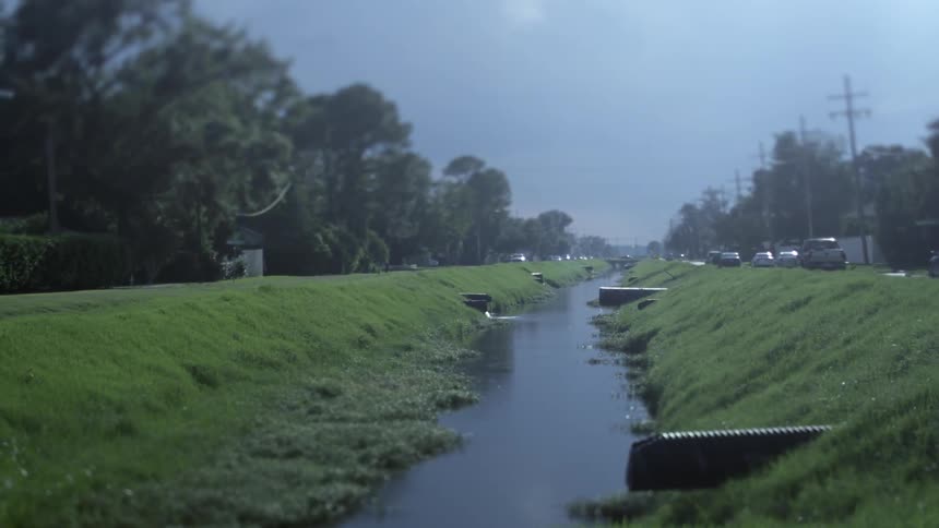 Cars drive past a drainage ditch during the day