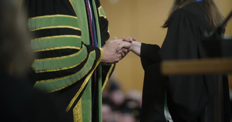 A woman who is graduating reaches out to receive a congratulatory handshake from a university administrator