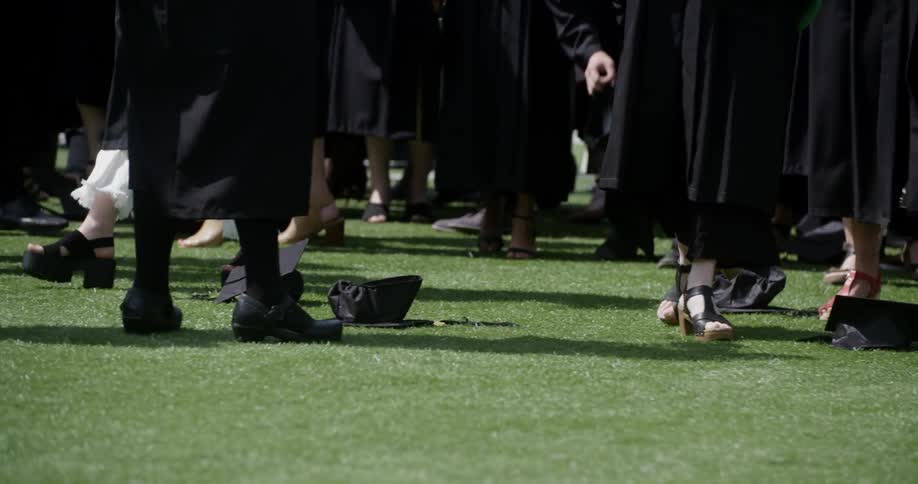 Graduate walk along the grass and pick up their caps