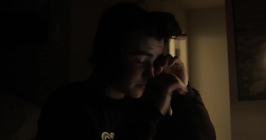 A student lifts his head from his desk rubs his eyes and goes back to work on his laptop