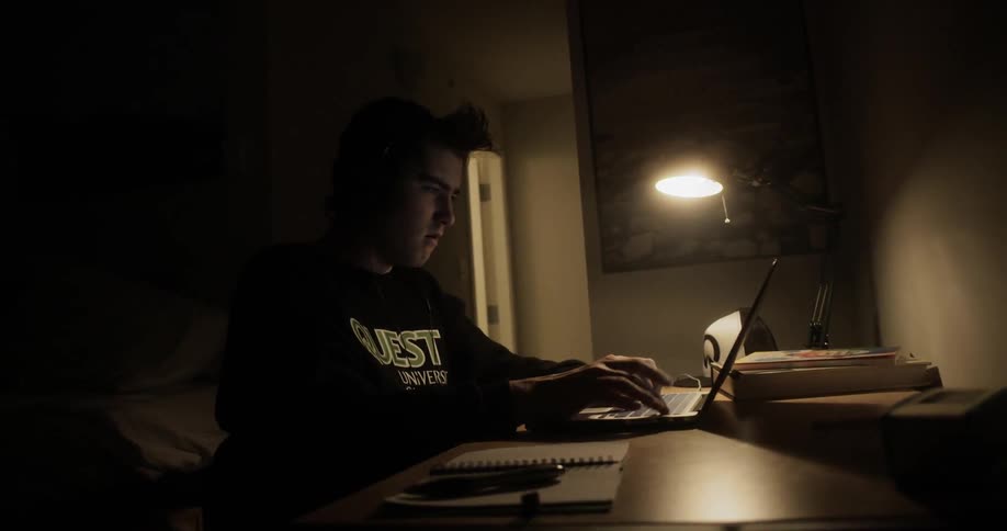 Boy sleeping at the desk wakes up and uses laptop in the dark room