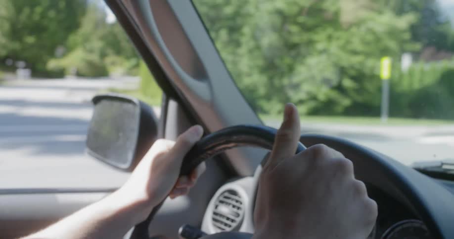 A man taps his thumbs on a steering wheel as he drives