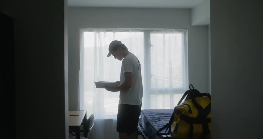 Man holding a book to read sits down on bed in a room