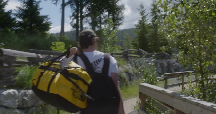 Man carrying backpacks walks on the walking trail next to the fence on a windy day