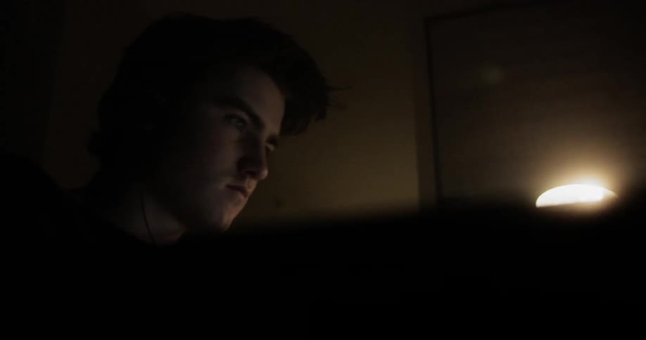 Man sitting at the desk uses laptop in a dark room