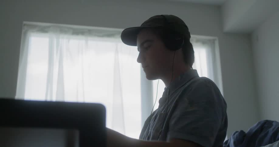 A teenager is sitting at his desk with a headset on