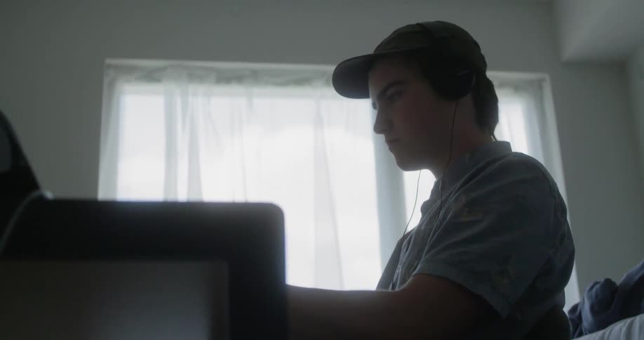 Teenage boy sitting at his desk listening to music in his room