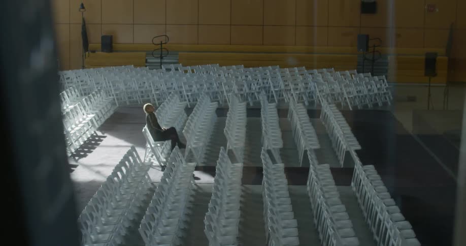 A lone person sitting in the chairs of an auditorium