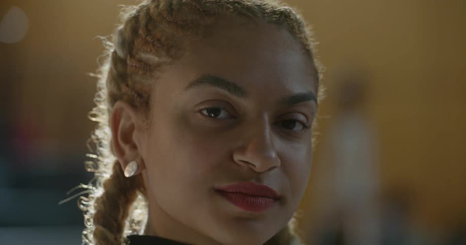 A woman with braided hair turns her head and looks directly into the camera with confidence