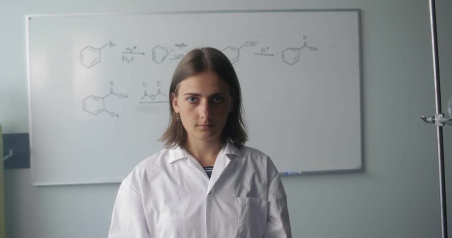 A young woman stands at the front of a class in a lab coat