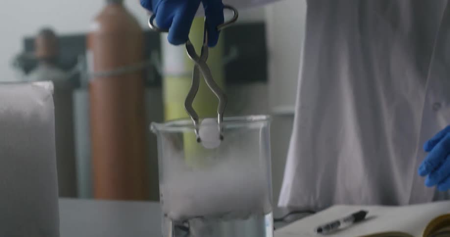 Person uses tongs to place dry ice in beaker mixture