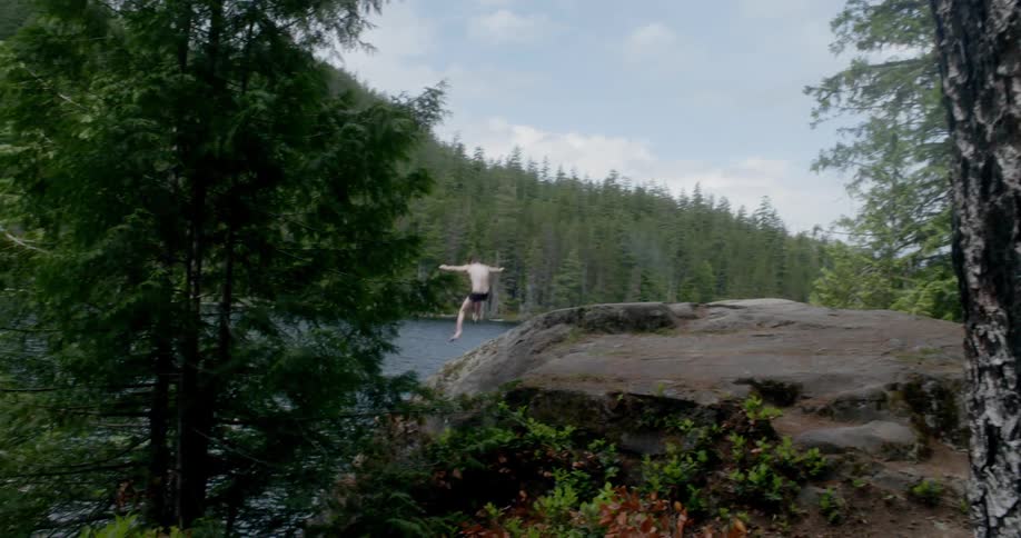 Man jumping off a large rock into a lake in the forest
