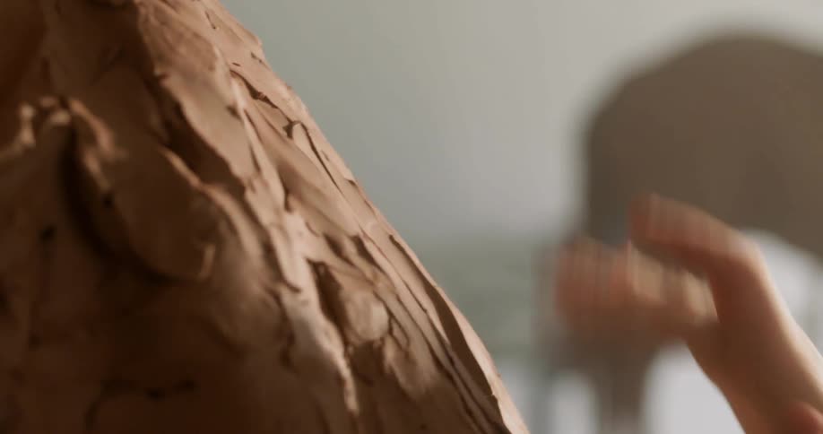 A woman rubs her hand on the sculpture she is working on