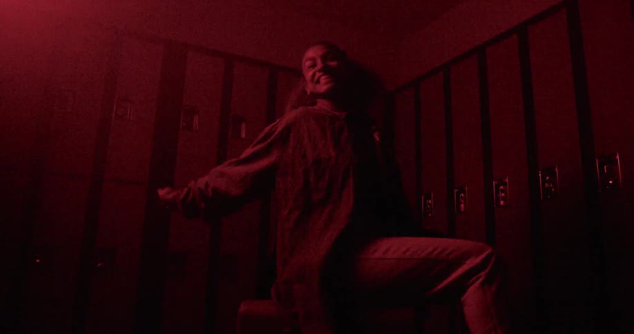 A black girl poses wildly while sitting on a cube in front of a row of lockers