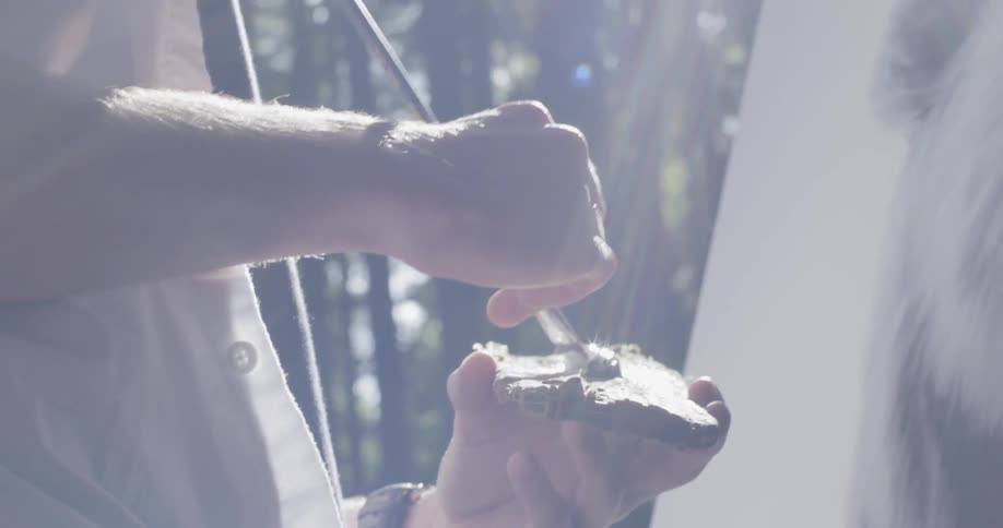 A man rubs his paintbrush on some wood before painting