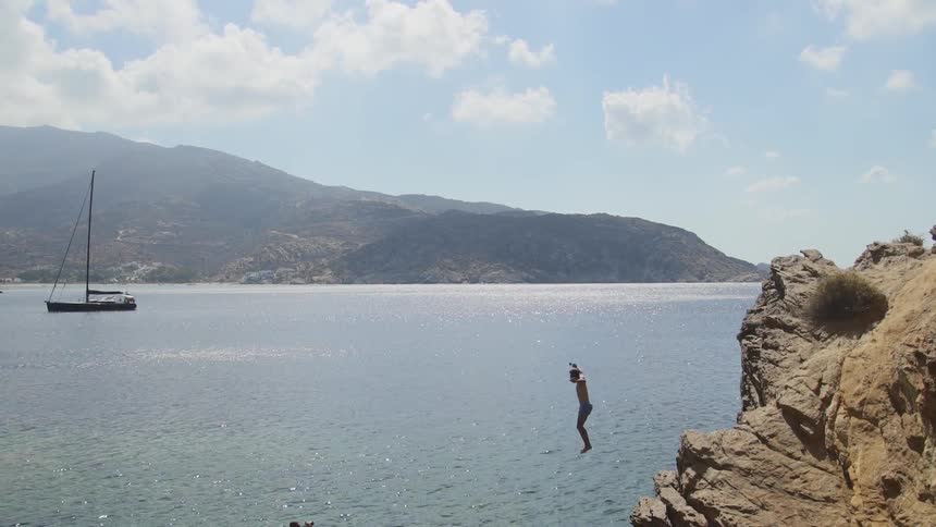 A young man jumps off a cliff in to the water below