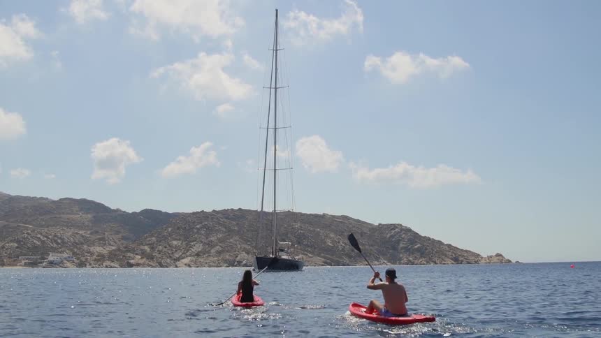 Man and woman kayaking towards a sail boat in the ocean