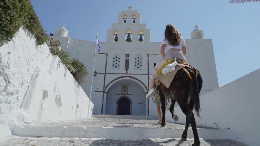 A man pulls a donkey while a woman sits on it in greece