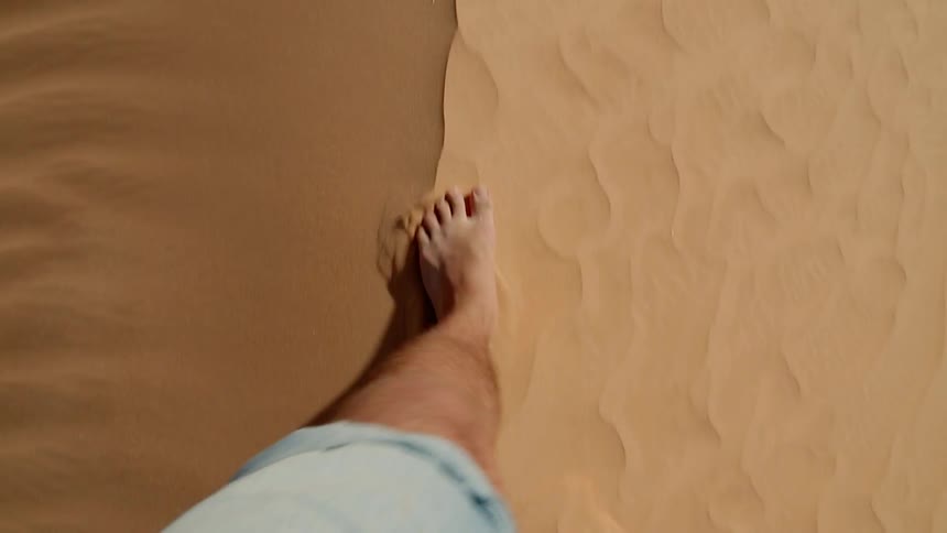 A man walks on a sand dune barefoot