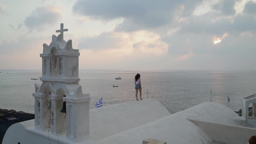 A young woman walks along the roof of an old church next to the ocean