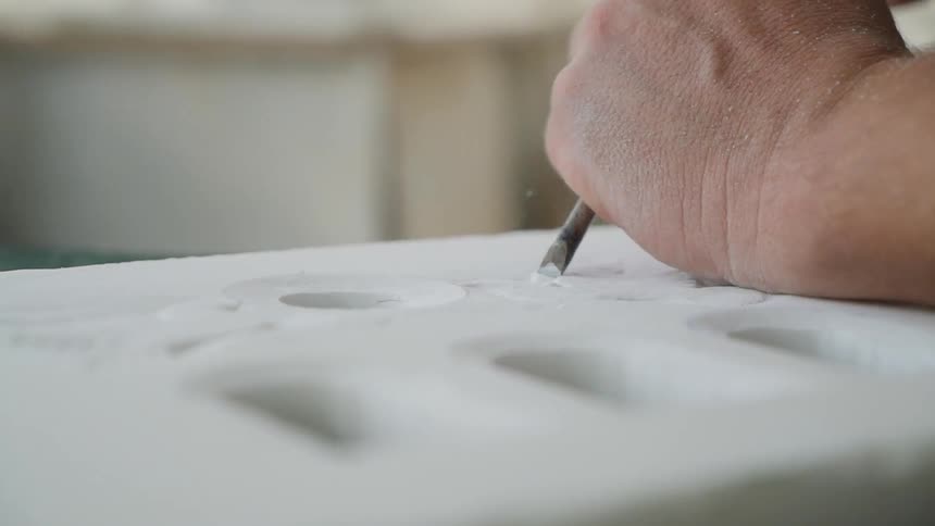 A person uses a chisel on an object to create holes