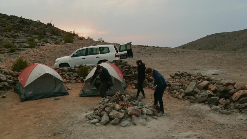 Three campers carry supplies including wood for the fire to a campsite