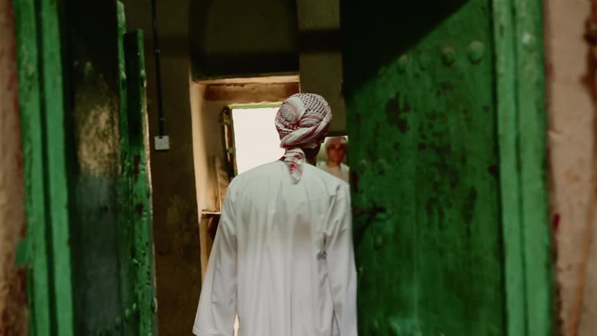 A middle eastern man in a robe walks through the doors of a building